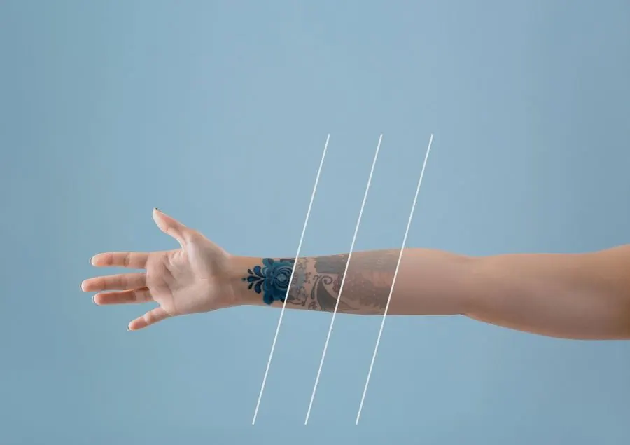 Extended arm with tattoos reaching against a light blue background, with three white lines crossing the arm at different points.